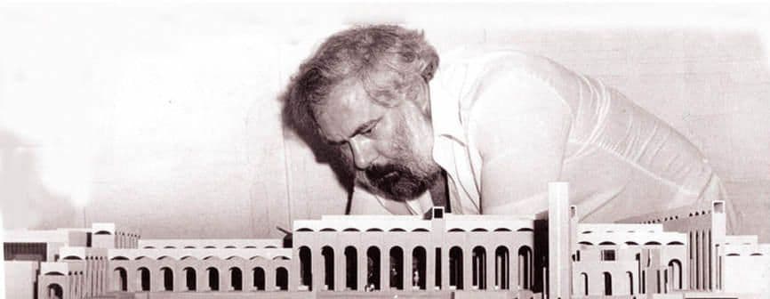 Man with beard intently examines a detailed architectural model with arched facades.