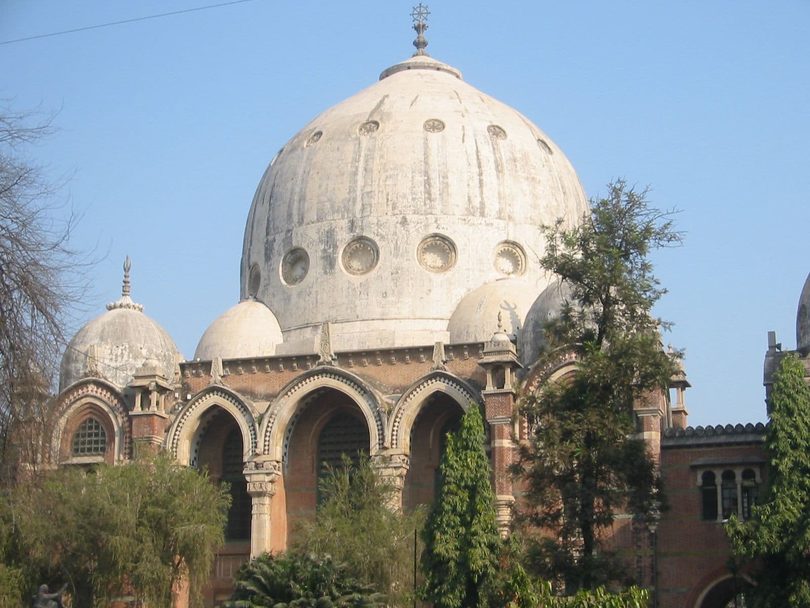 Large white dome building with arched windows and surrounding trees against a clear blue sky.