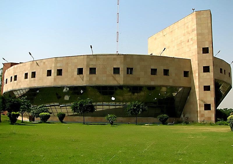 Modern concrete building with a curved facade and rectangular windows under a clear blue sky.
