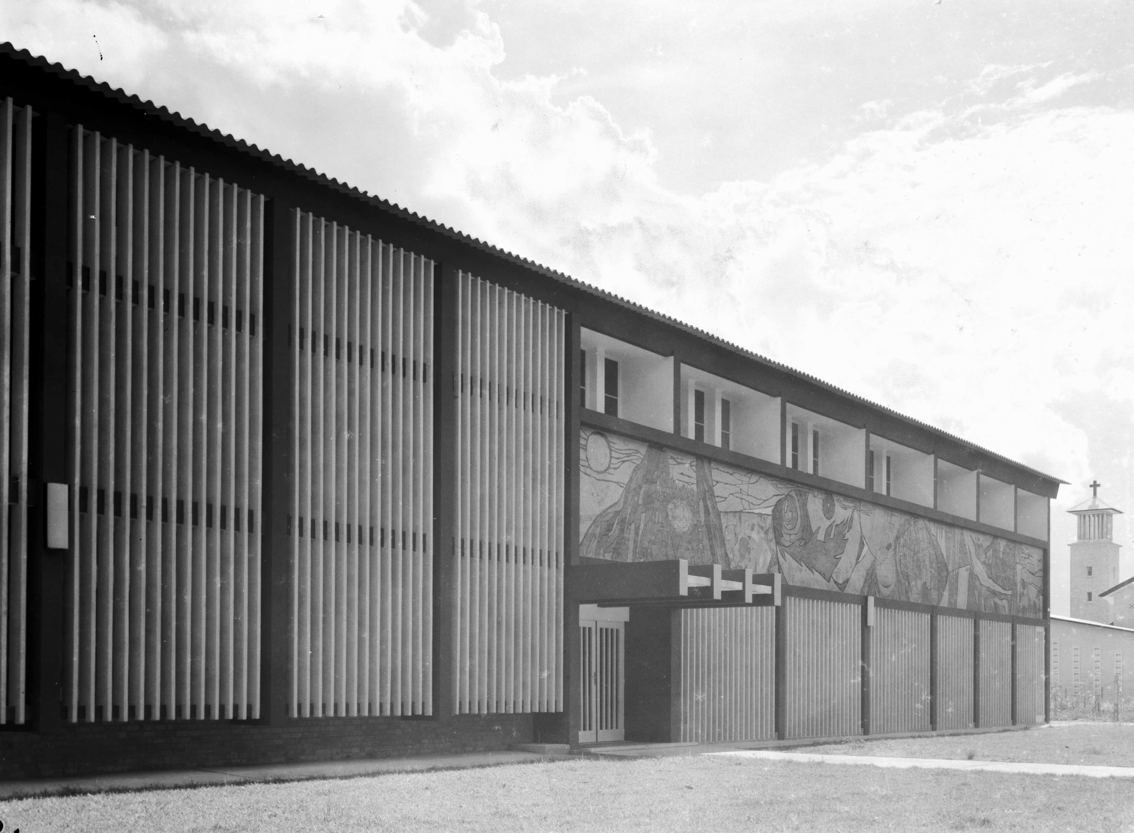 A modern building with a long facade featuring vertical louvers and large glass panels showcasing stained glass.