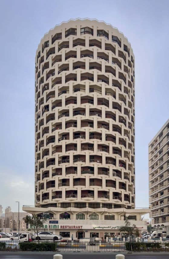 A tall, cylindrical building with many small, repeating arched windows under a clear sky.