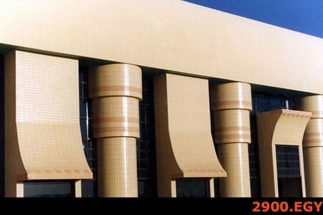 Modern building facade with large tan, curved, and cylindrical architectural elements.