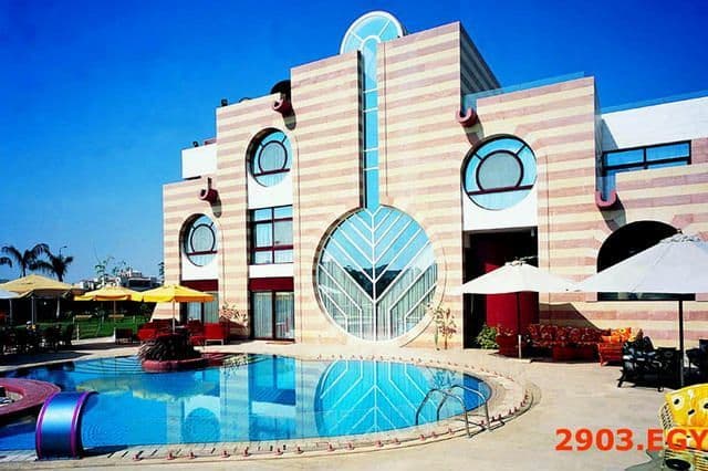 Modern building with striped facade, circular windows, and a large glass design beside a pool.