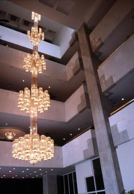 Tall, multi-tiered crystal chandelier illuminating a spacious modern atrium with multiple levels.