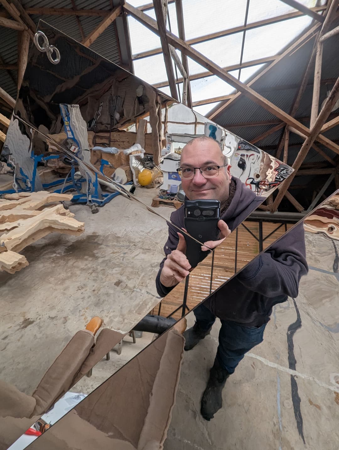 Man in glasses holds up a reflective surface in a workshop.