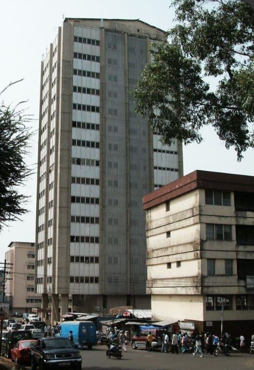 Tall grey building stands over a busy city street with people and vehicles.