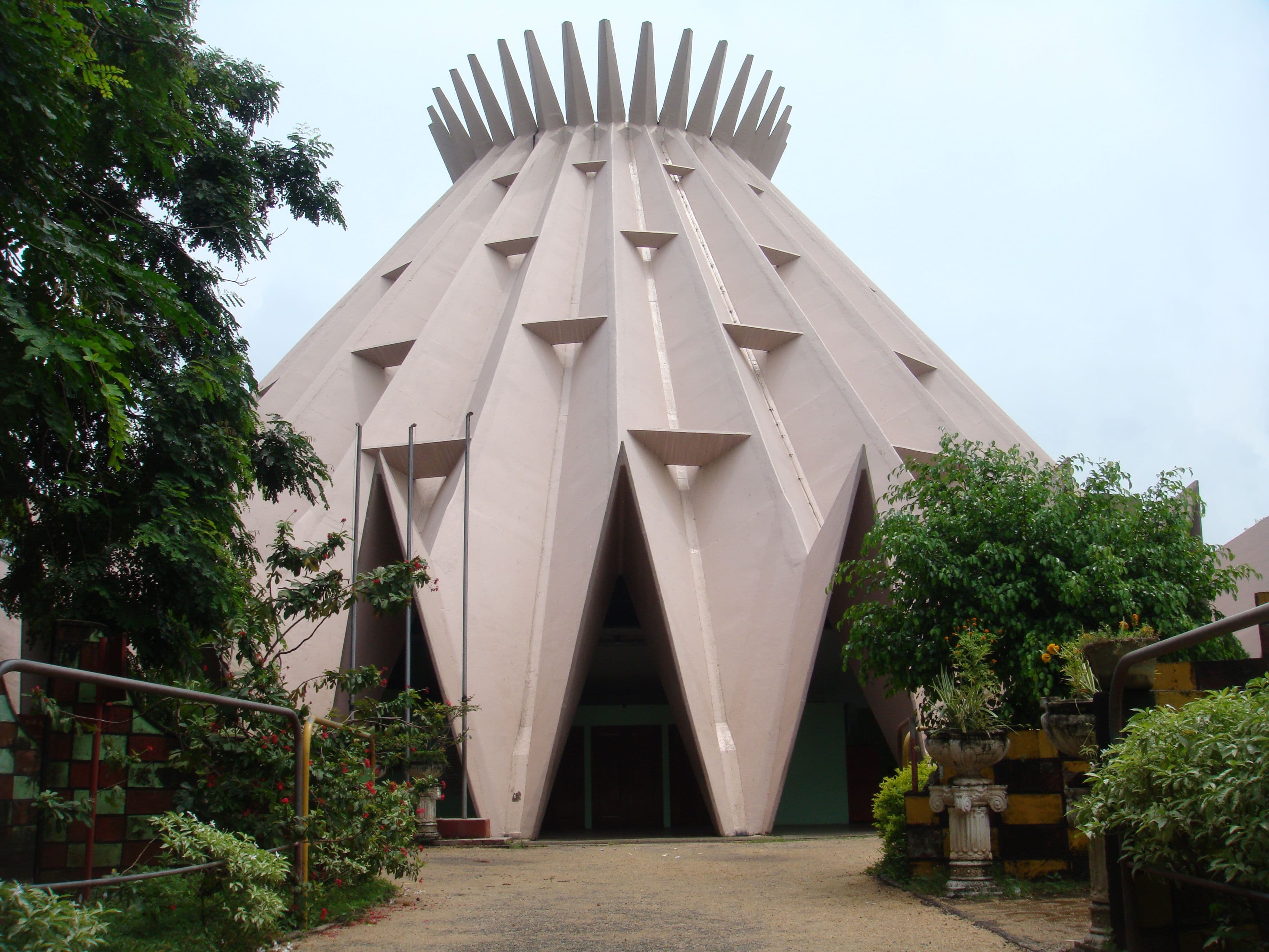A unique, conical building with ribbed sides and a spiky crown against a grey sky.