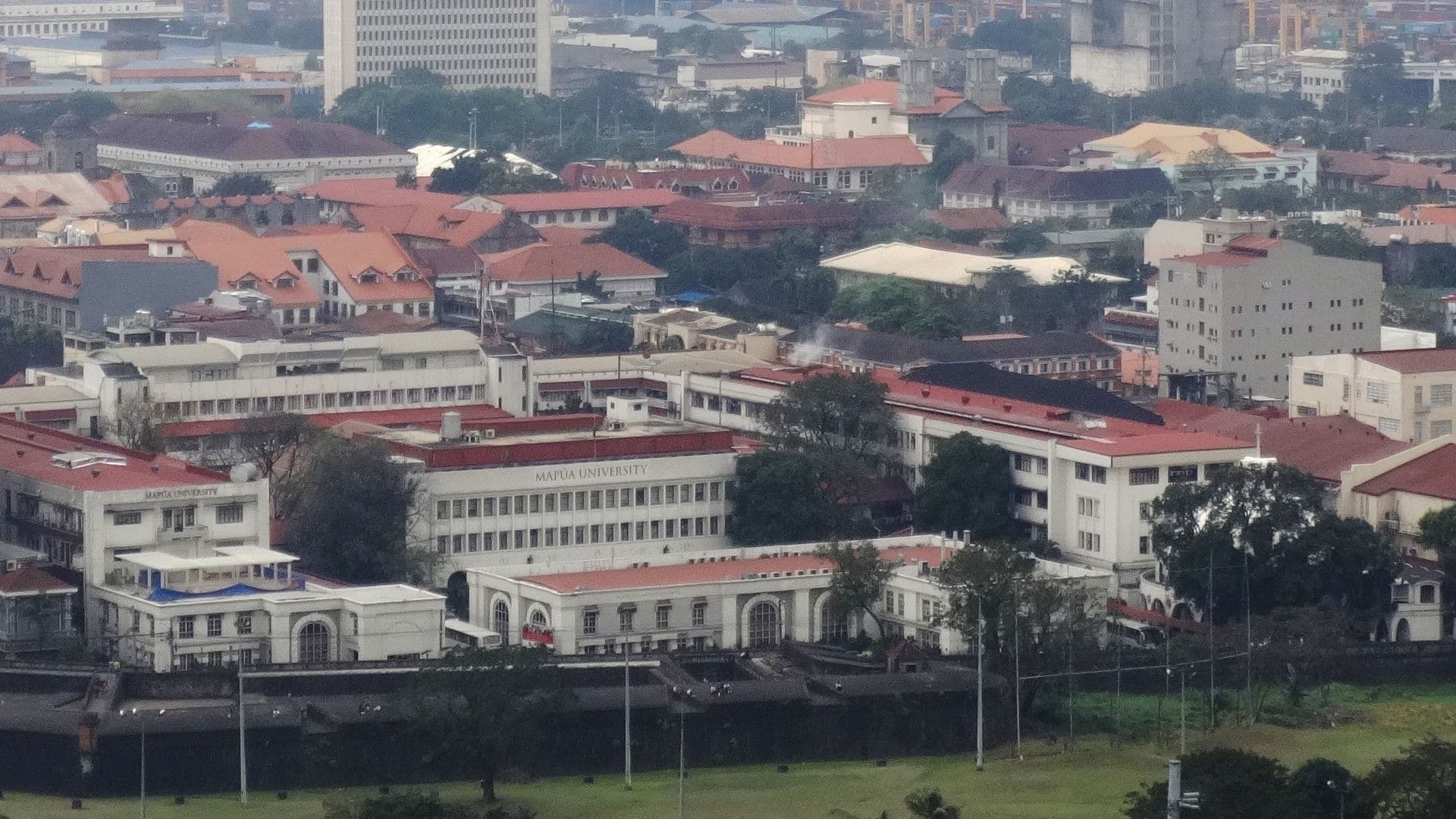 Panoramic view of a sprawling cityscape with numerous buildings and trees under a hazy sky.