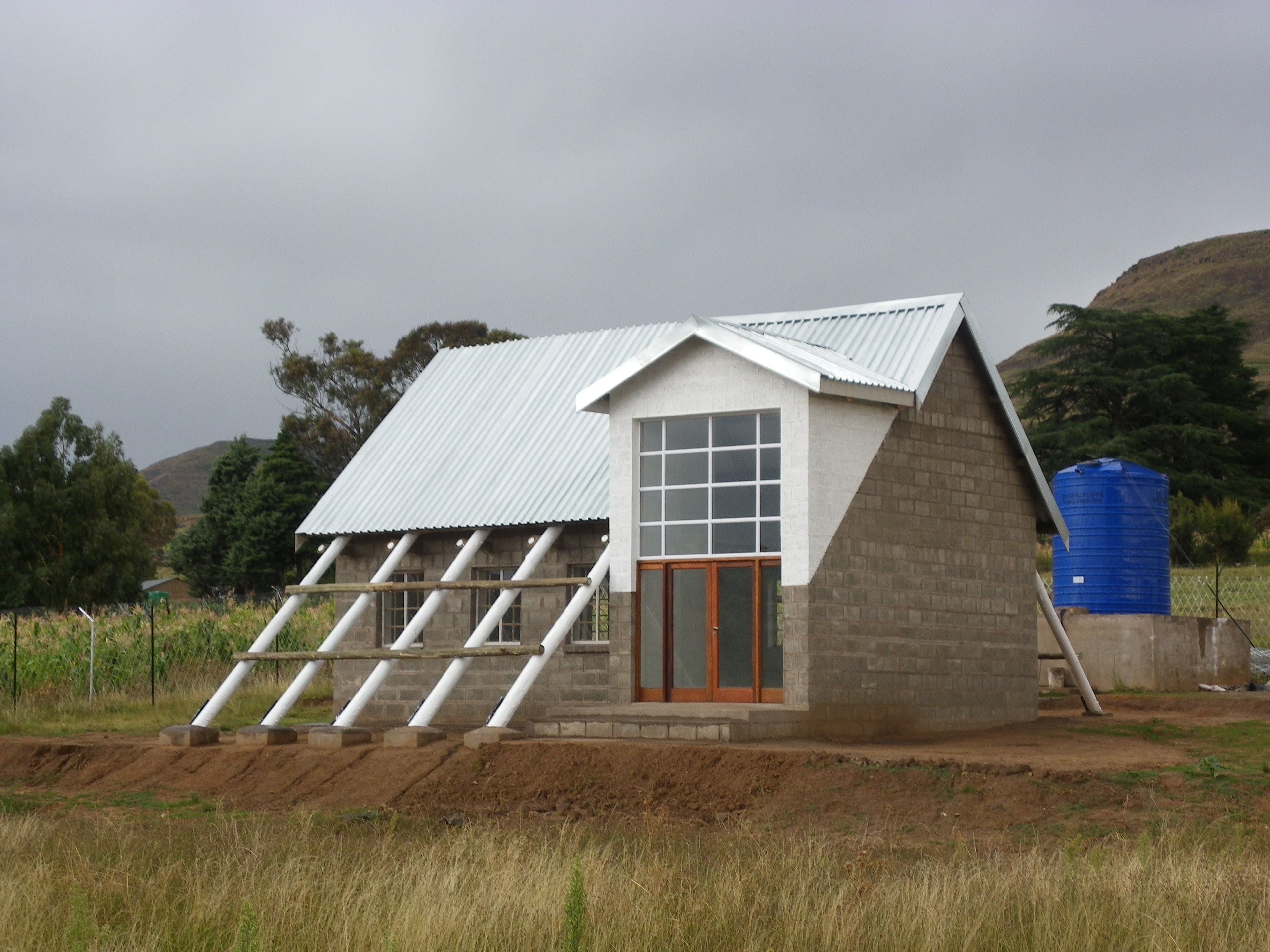 Modern angular house with metallic roof, brick walls, and large windows in a rural setting.