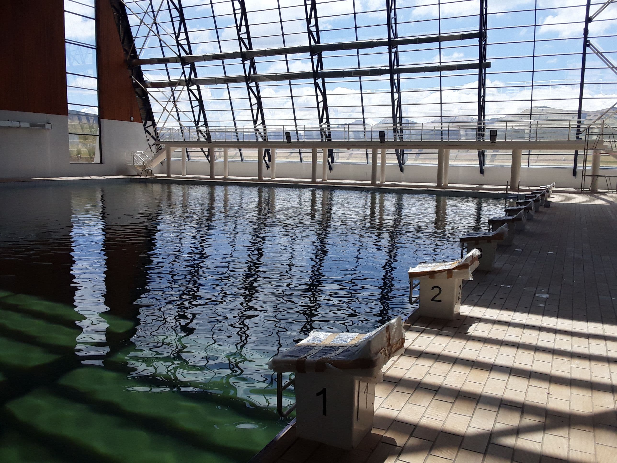Indoor swimming pool with starting blocks and a modern glass ceiling reflecting light.