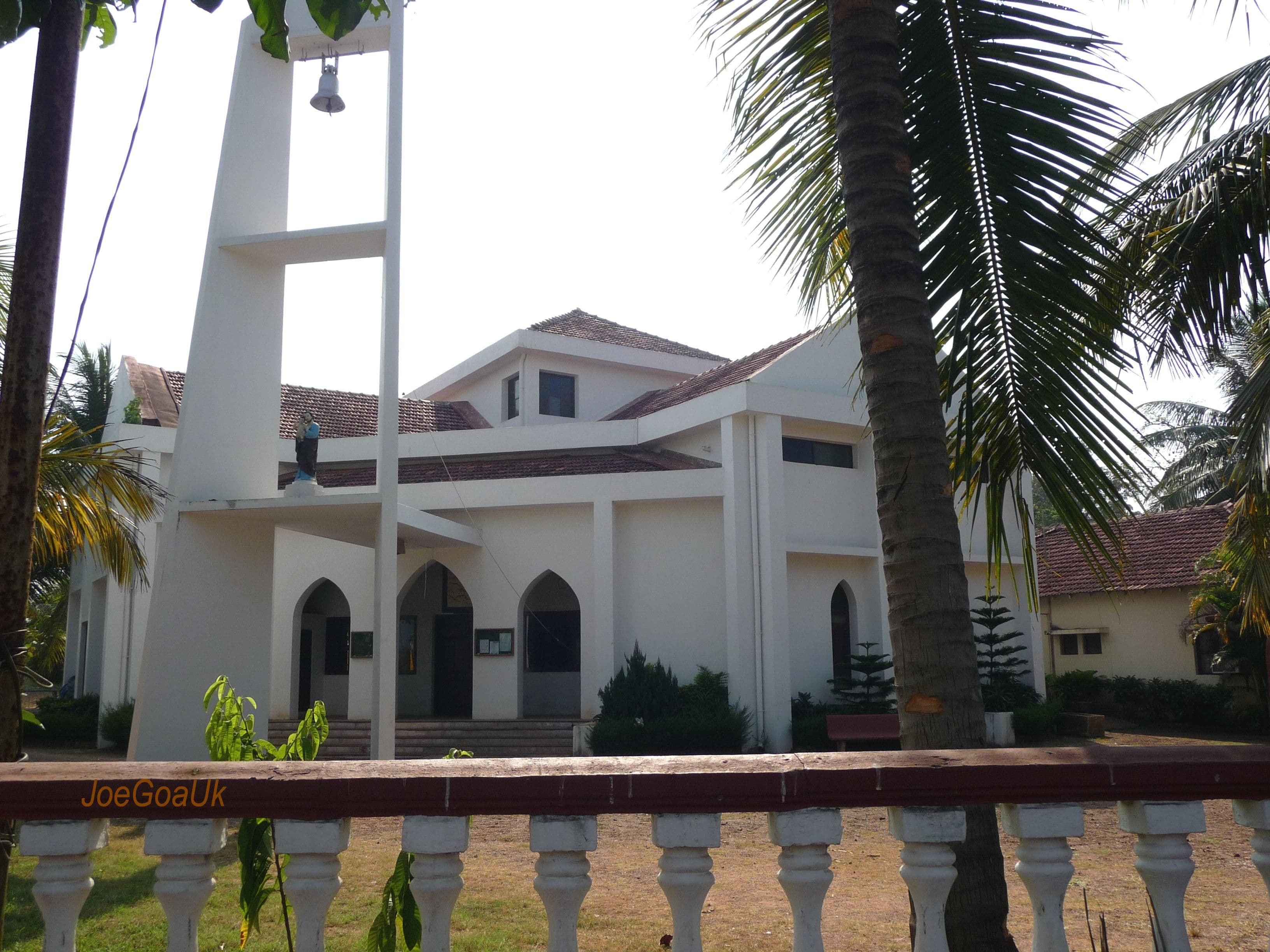 Modern white church with a tall bell tower and red-tiled roof, framed by palm trees.