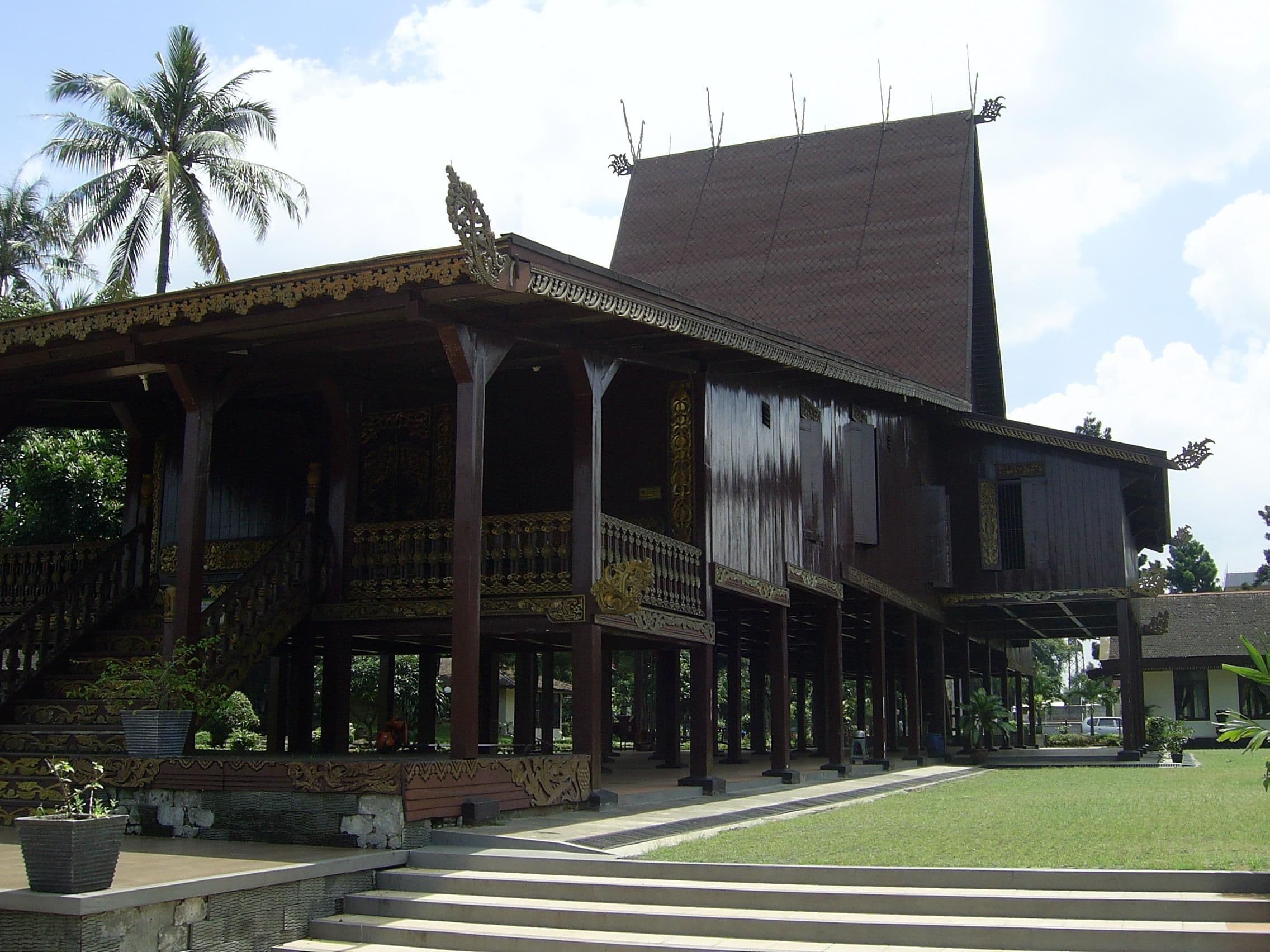 Traditional wooden stilted house with a tiered, dark roof and intricate carvings.