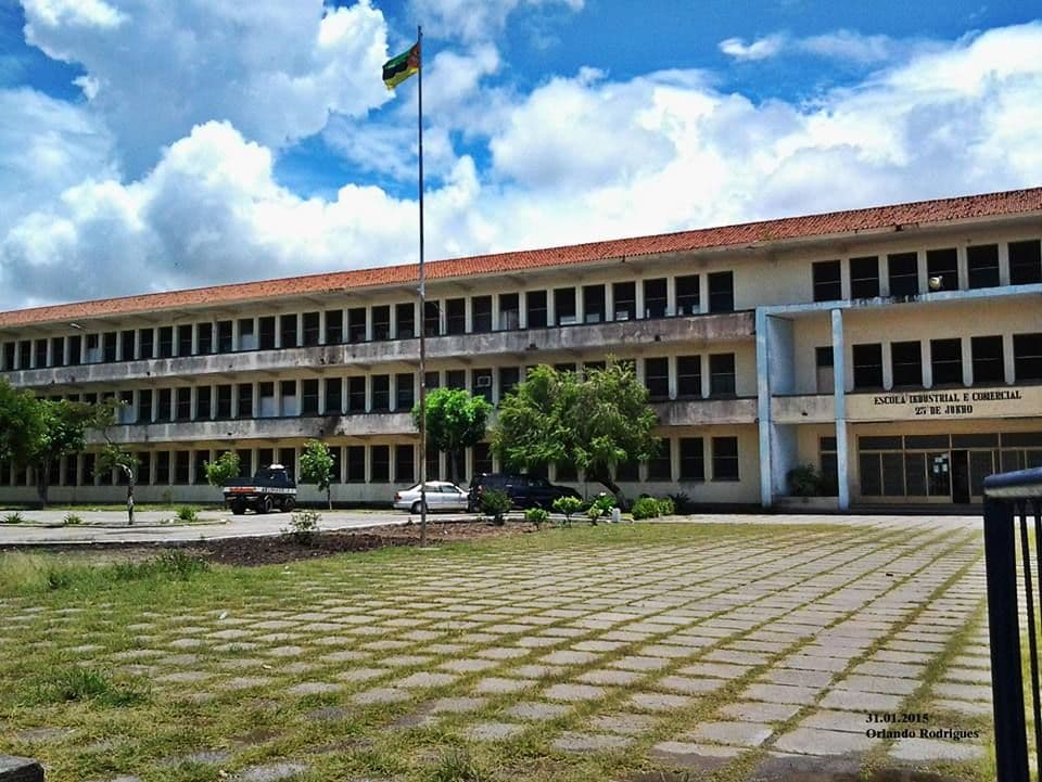 A large, multi-story building with a flag pole in front under a cloudy sky.