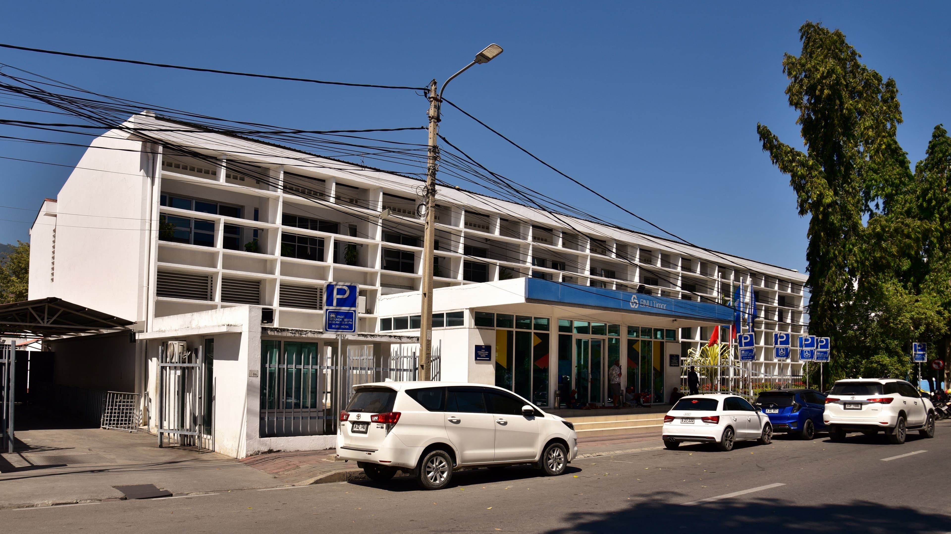 A long, white, multi-story building with blue trim and many windows, parked cars in front.