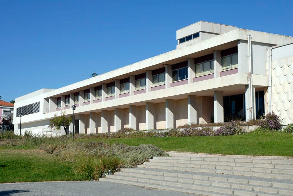 Modern building with a long white facade and shaded lower level walkway.