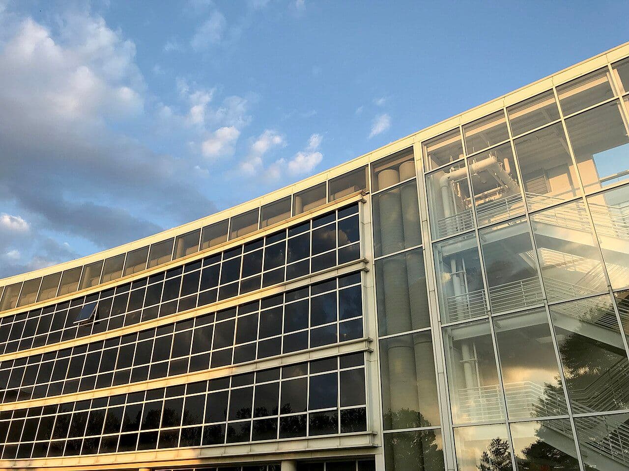 Modern glass building with repeating windows under a cloudy sky.