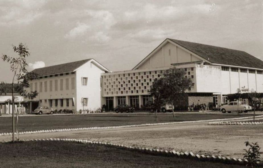 A large mid-century building with a decorative facade and a spacious lawn.