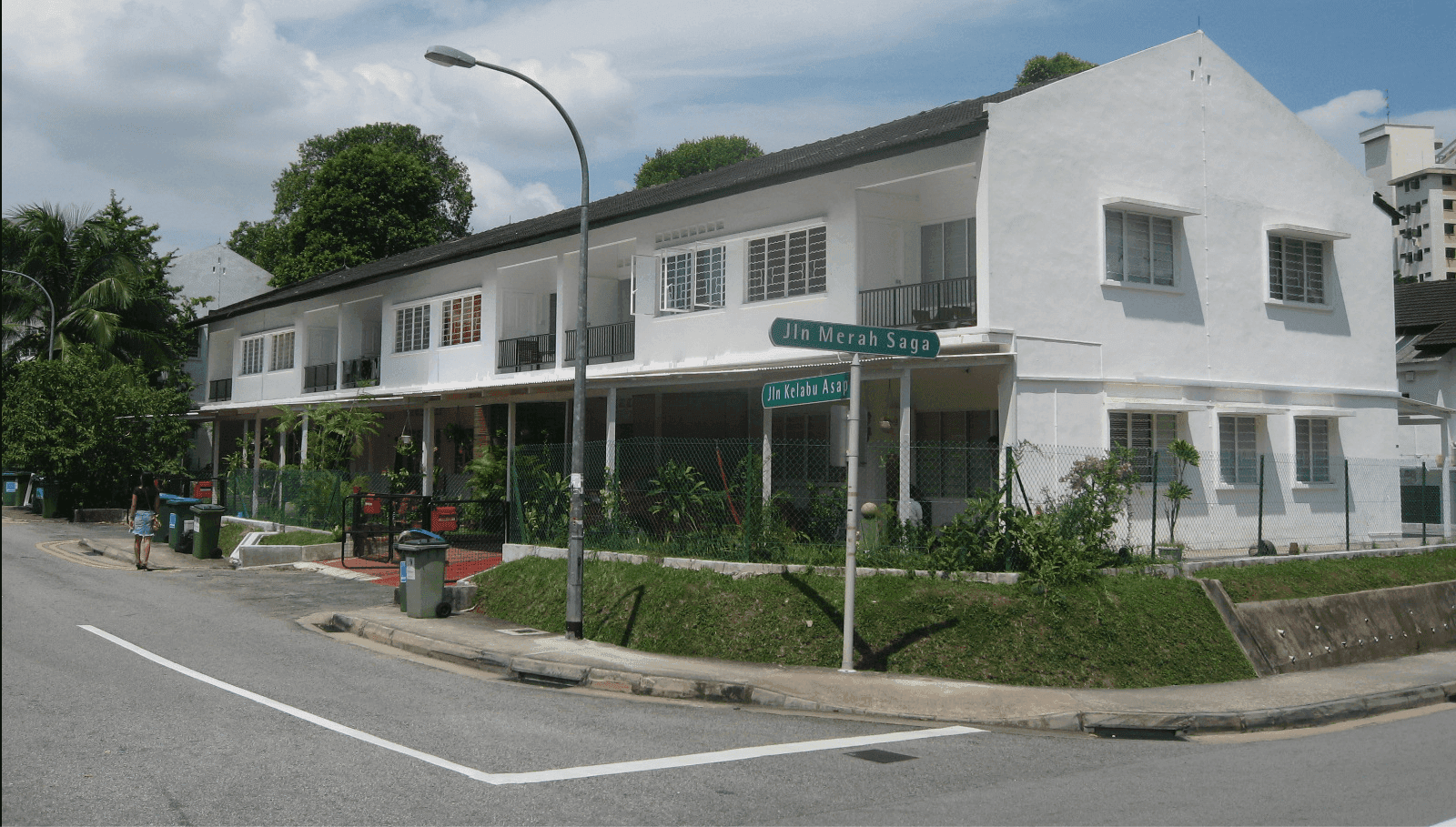 White terraced houses with green lawns and trees on a street corner.