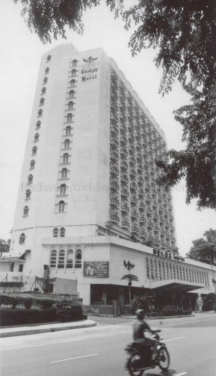 Tall, angular hotel building with many windows, seen from street level with trees and a motorcycle in foreground.