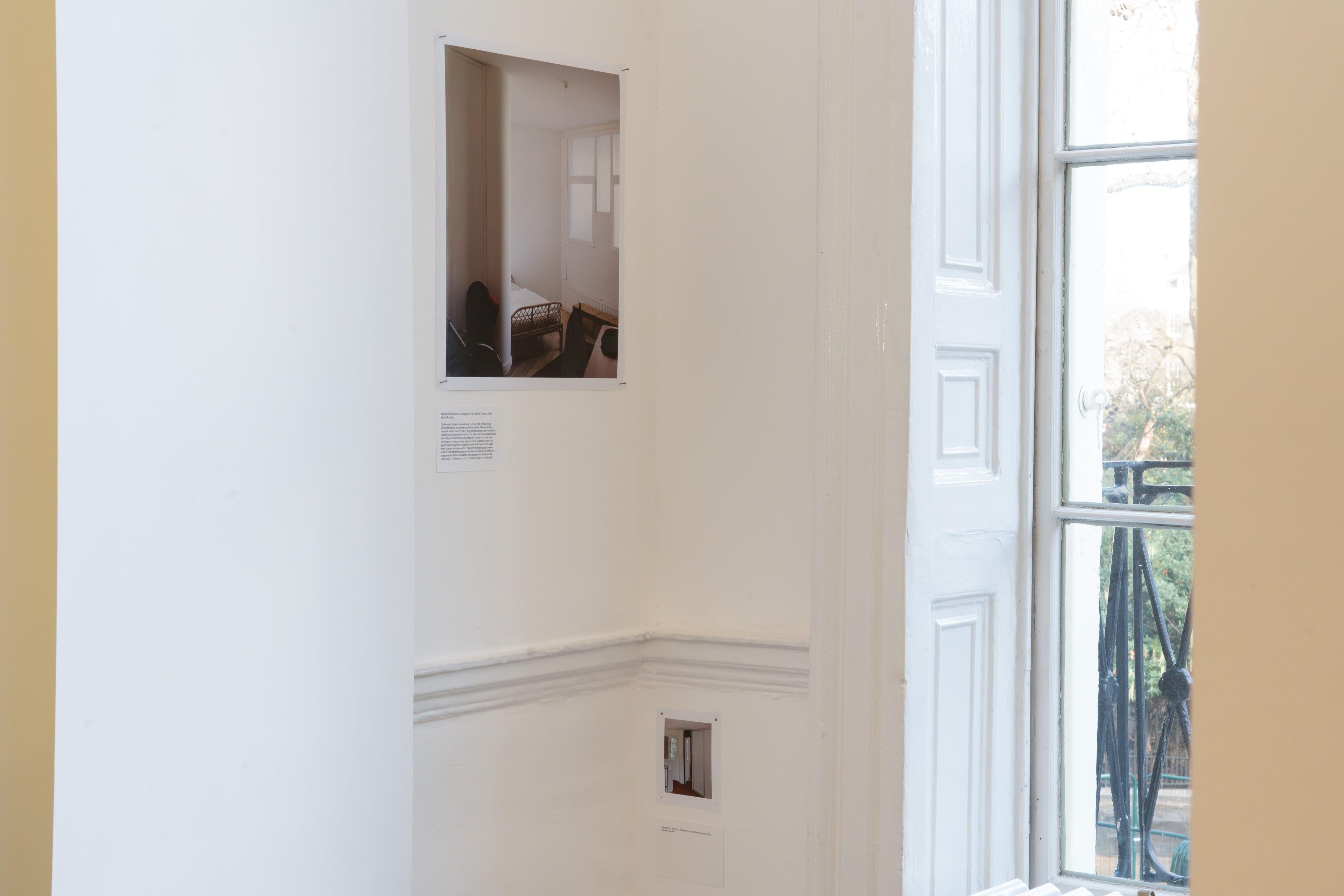 A photo is mounted on a white wall next to a window with Georgian shutters at its side.