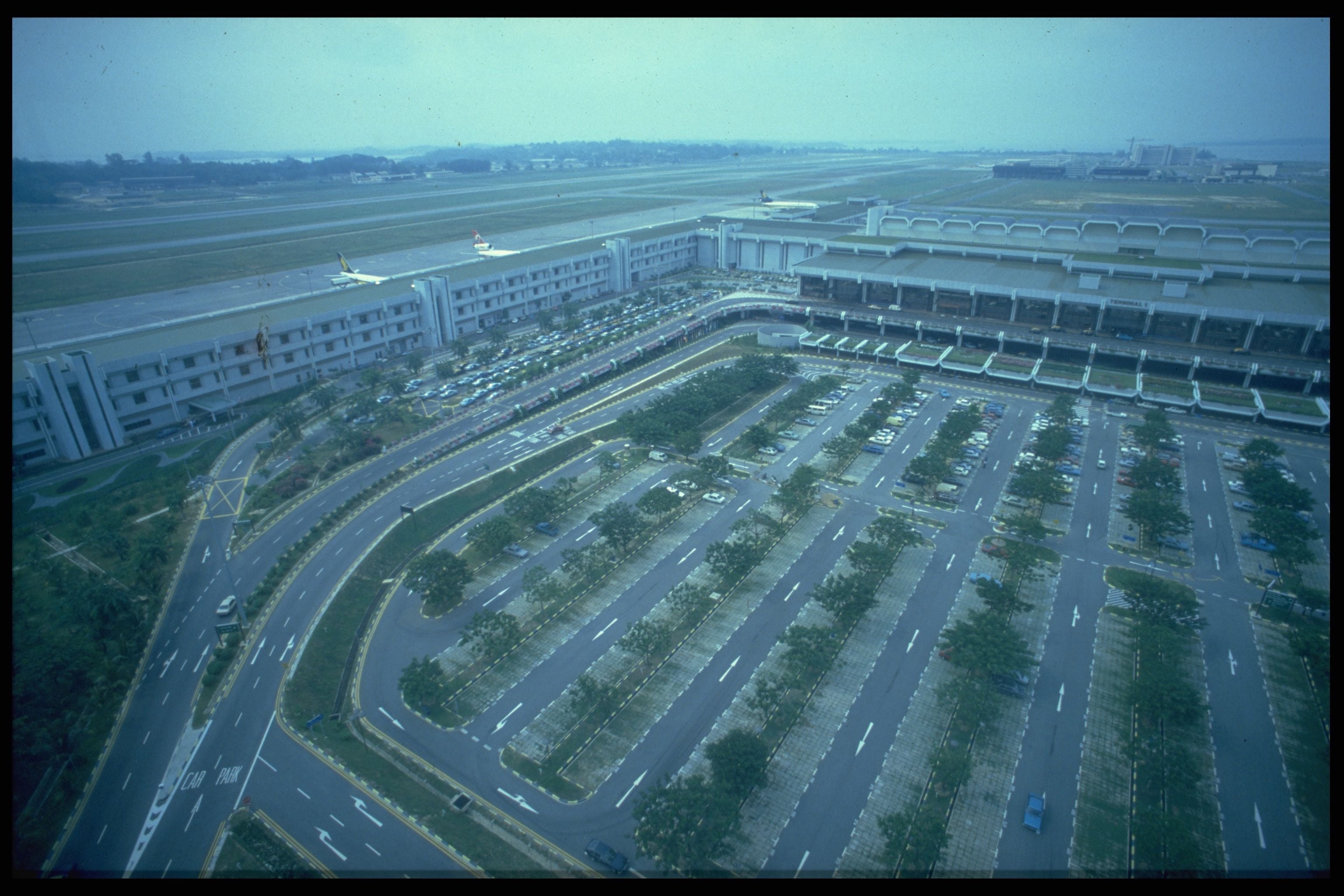 Aerial view of a large airport with runways, a terminal building, and extensive parking lots.