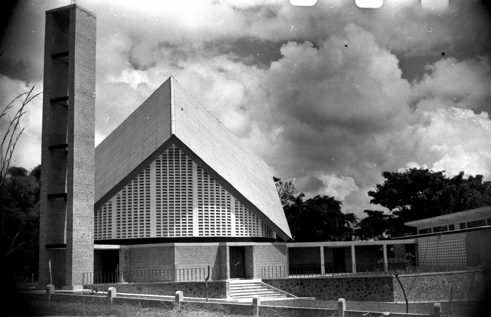 Modernist church with a tall, slender bell tower and angular rooflines against a cloudy sky.