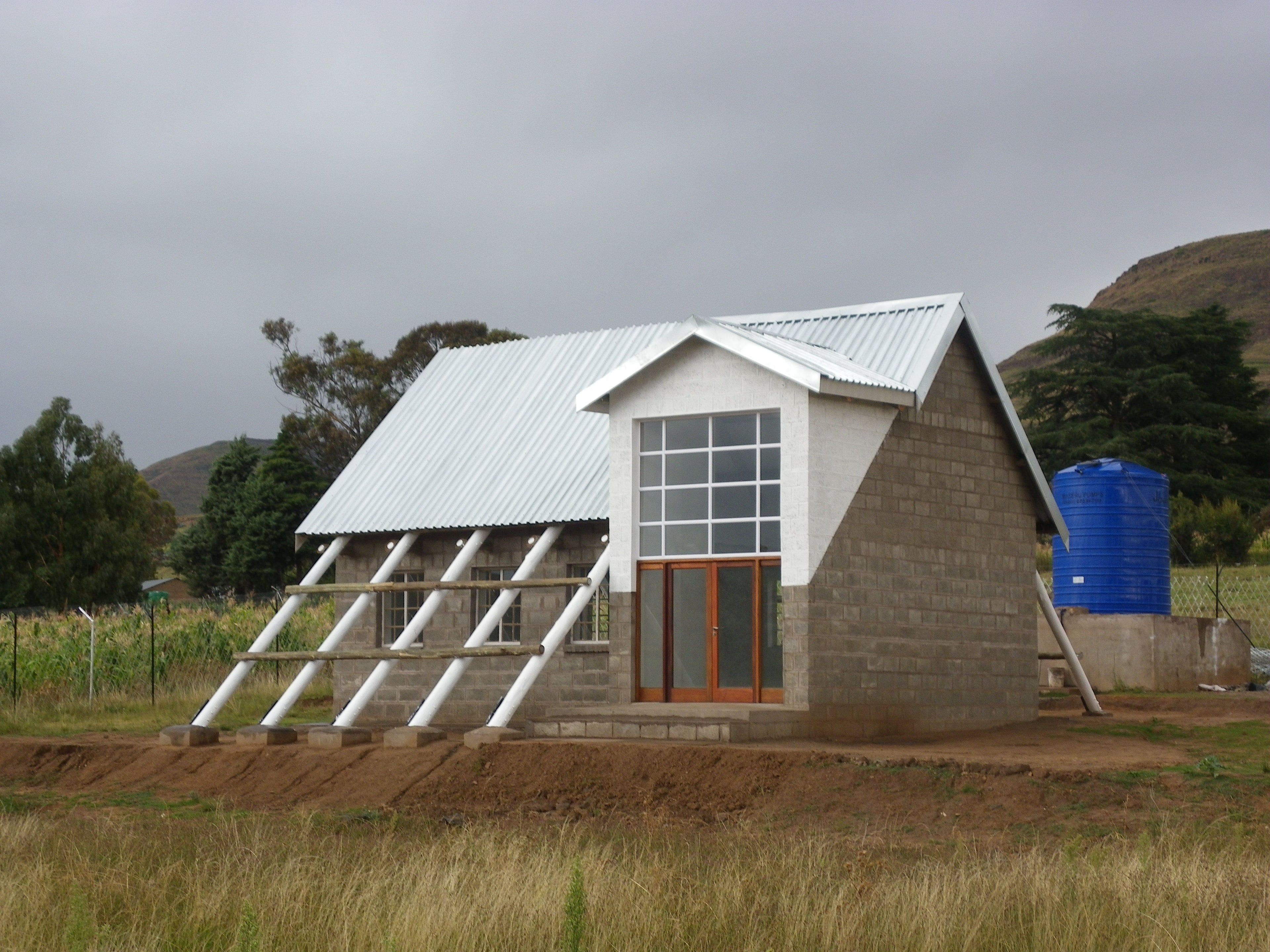 Modern angular house with metallic roof, brick walls, and large windows in a rural setting.