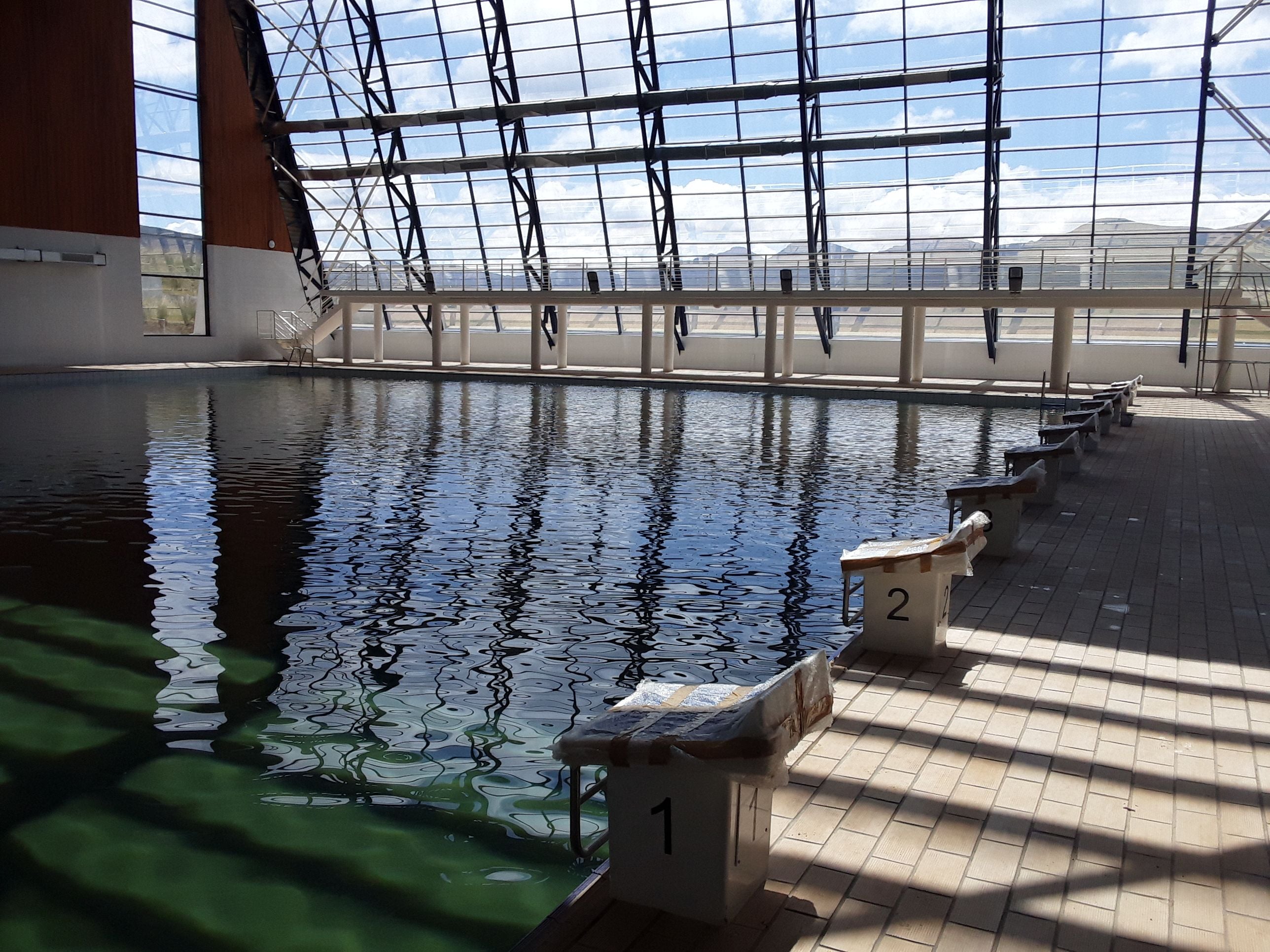 Indoor swimming pool with starting blocks and a modern glass ceiling reflecting light.