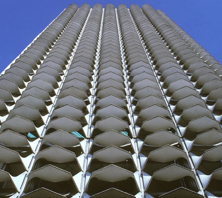 A modern building facade featuring repetitive geometric patterns against a clear blue sky.