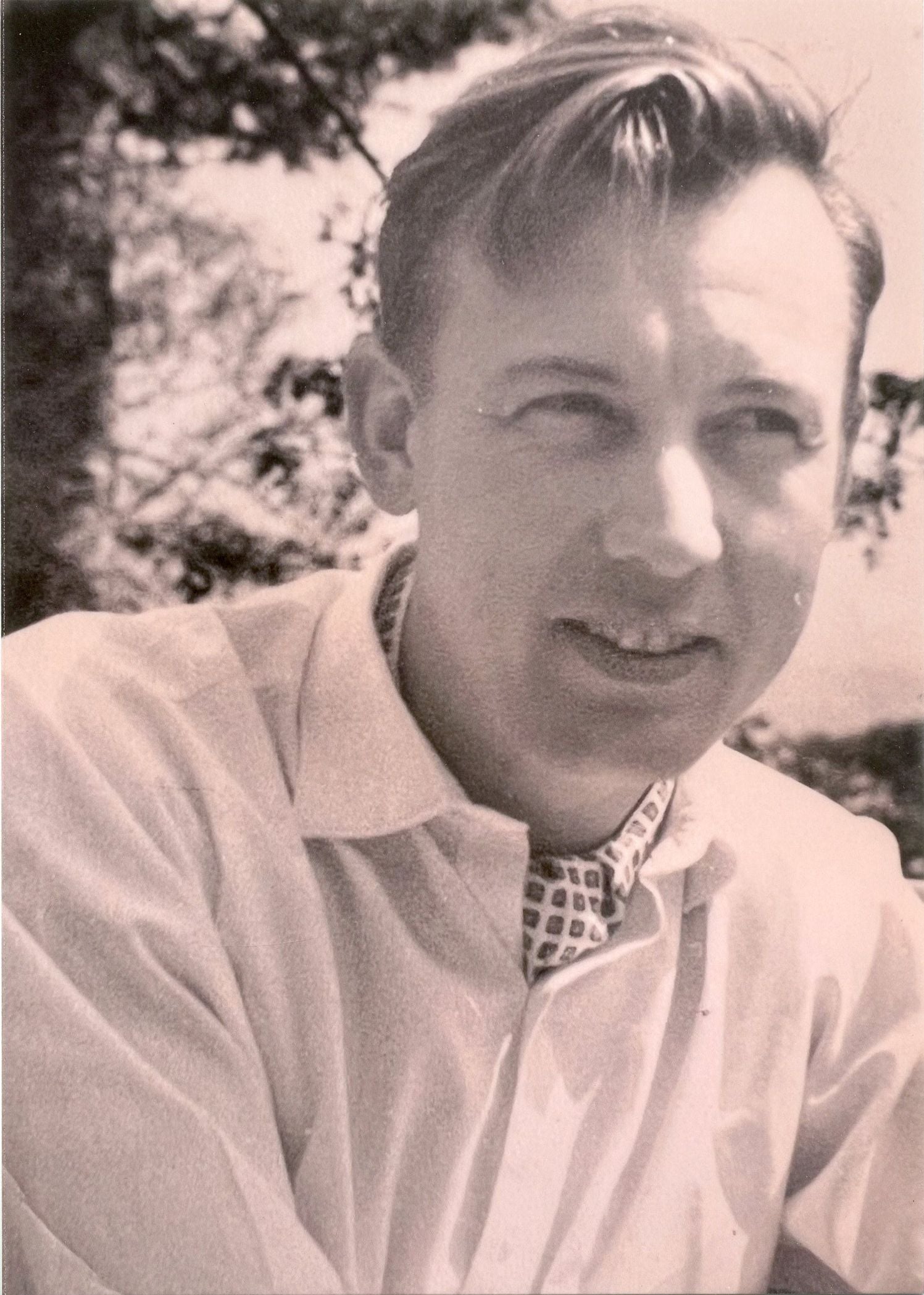 A man with short, light brown hair and a checkered tie smiles.