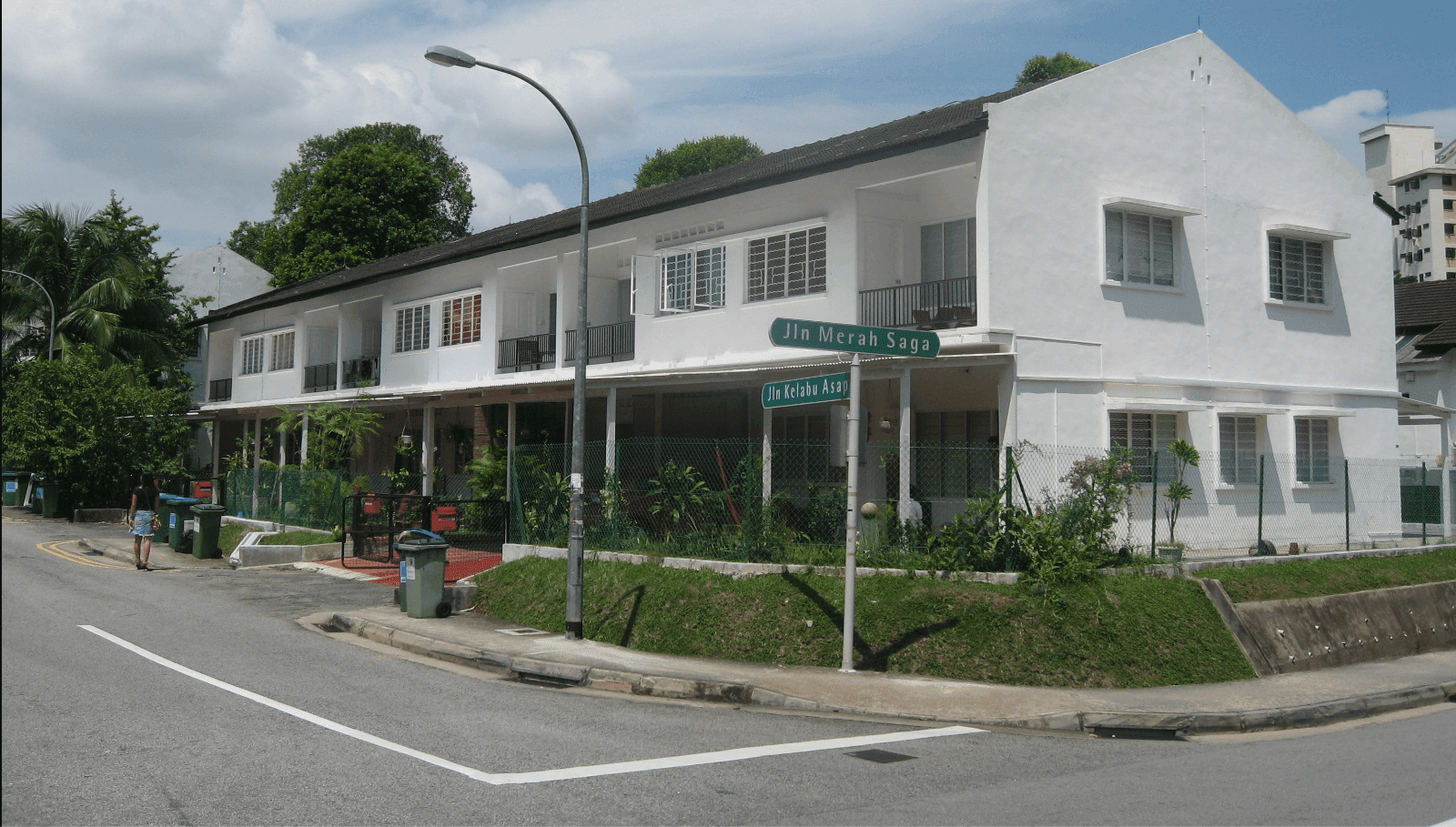 White terraced houses with green lawns and trees on a street corner.