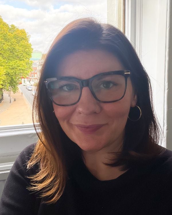 A woman with glasses and dark hair smiles at the camera.