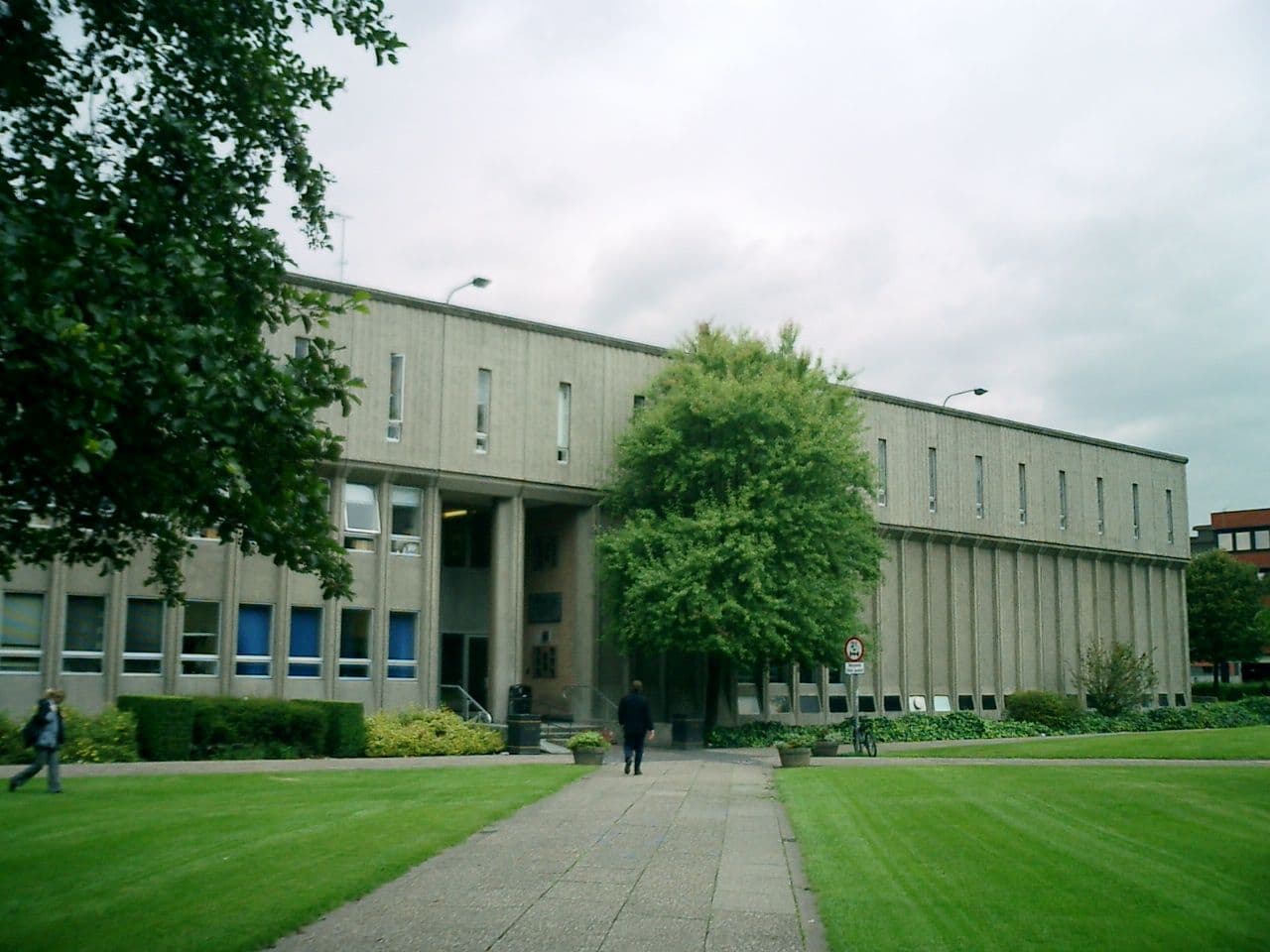 A large, modern concrete building stands behind a green lawn and paved path.