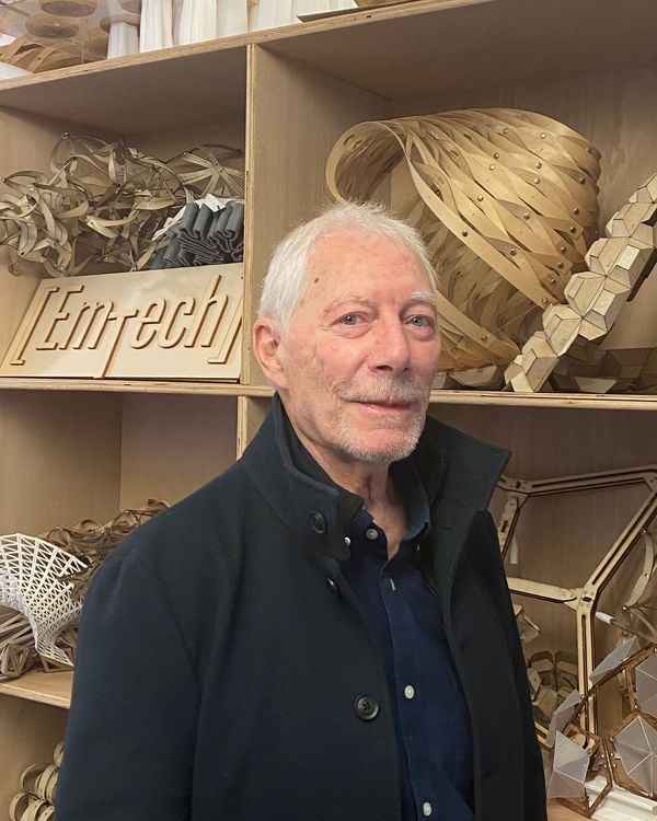 An older white man with short gray hair and a navy jacket stands in front of shelves.